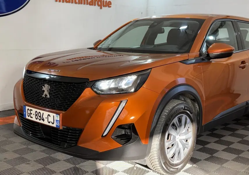 Vue 3/4 avant droit d’un Peugeot 2008 orange 2022 avec calandre noire et phares LED allumés.