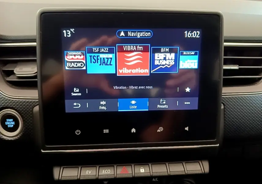 Écran tactile central de la Renault Arkana gris clair affichant les stations radio, avec bouton démarrage visible à gauche.