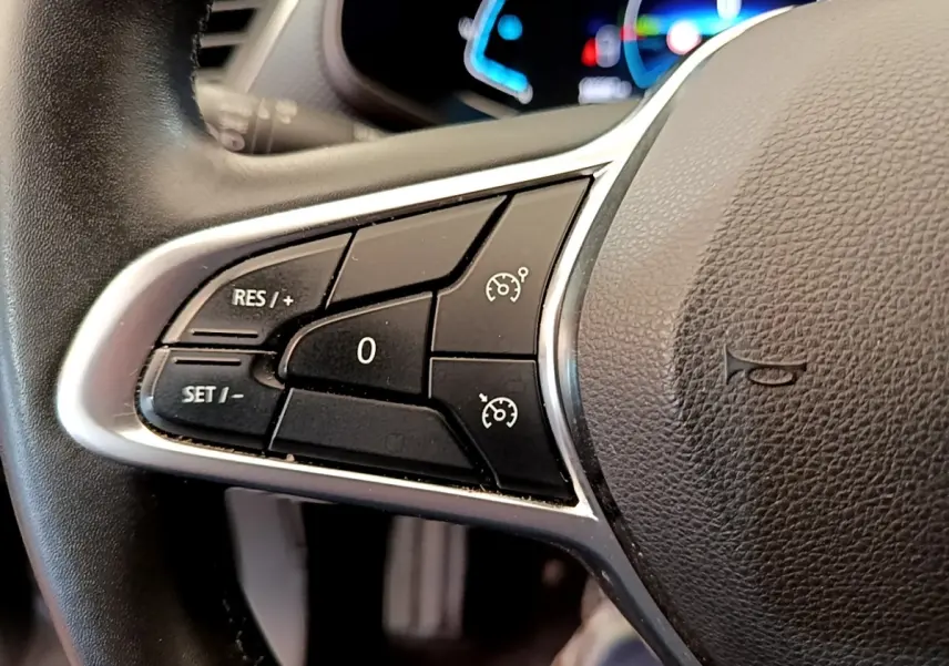 Gros plan sur les commandes de régulateur de vitesse au volant en cuir noir du Renault Arkana gris clair.