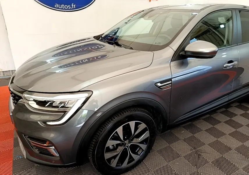 Vue 3/4 avant droit d’un Renault Arkana gris clair avec phares LED et jantes alliage distinctives.