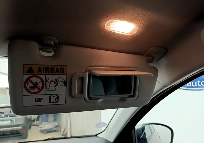 Détail intérieur montrant le pare-soleil côté conducteur gris clair avec miroir et avertissement airbag, éclairage allumé.