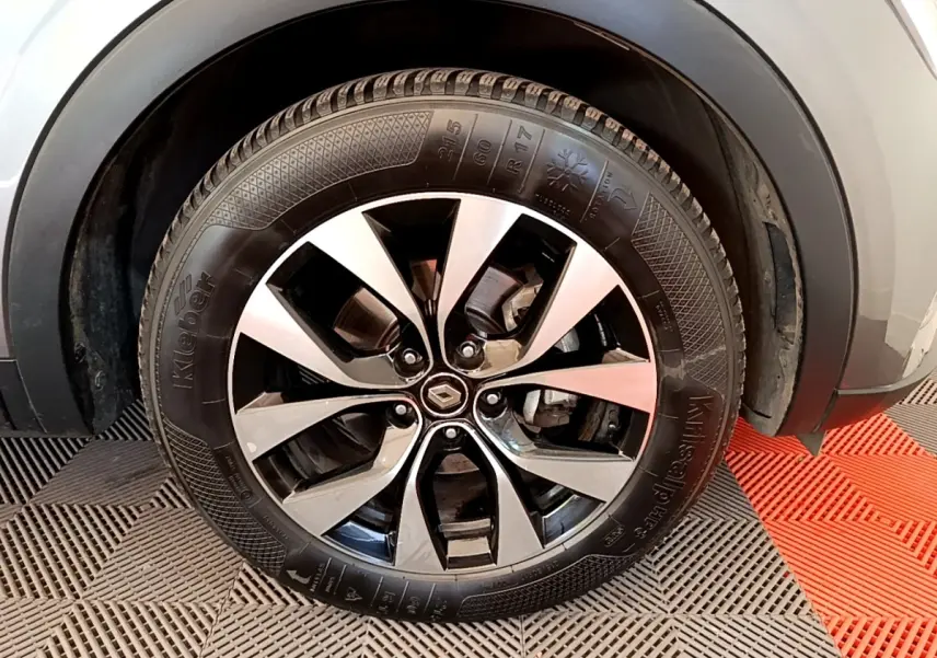 Gros plan sur la roue avant droite d’un Renault Arkana gris clair, jante alliage noir et argentée.