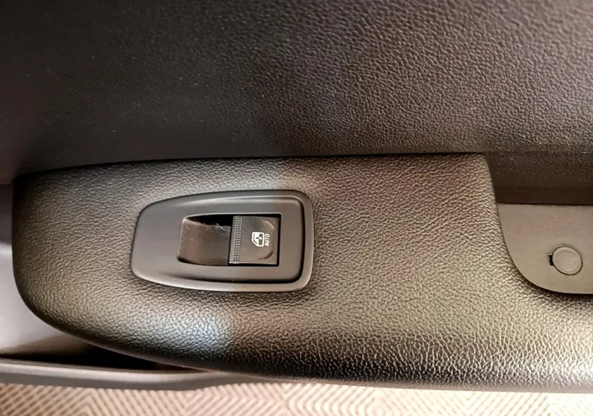 Gros plan sur le bouton de commande de la vitre électrique côté conducteur, intérieur noir texturé du Renault Arkana gris clair.