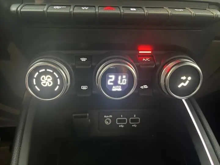 Gros plan sur les commandes de climatisation de la Renault Clio V blanc nacré, affichant 21°C en mode automatique.