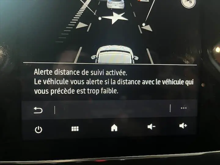 Affichage intérieur de la Renault Clio V blanc nacré métal montrant l'alerte de distance de suivi activée sur l'écran central.