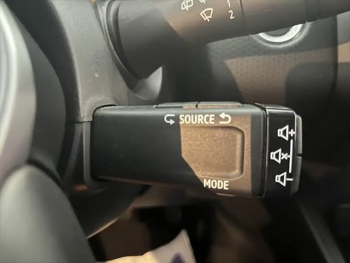 Gros plan sur la commande au volant de la Renault Clio V blanc nacré, avec boutons "Source" et "Mode" visibles.