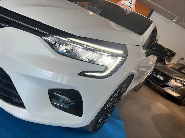 Gros plan sur l'avant droit d'une Renault Clio V blanc nacré métal avec phares LED allumés en showroom.