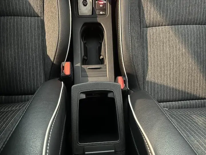 Vue plongeante sur la console centrale noire et les sièges gris rayés avec surpiqûres blanches d'une Renault Clio V blanche nacrée.