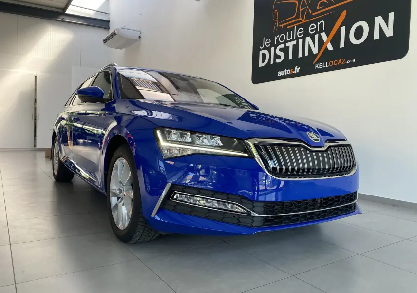 Vue 3/4 avant gauche d'une Skoda Superb Combi bleu énergie en showroom, soulignant ses phares LED et sa calandre chromée.