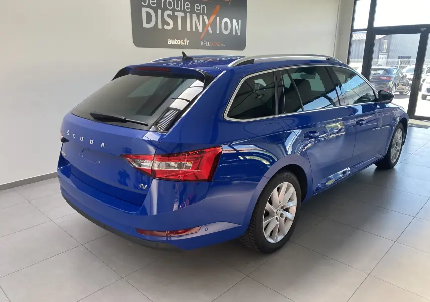 Vue 3/4 arrière droite d'une Skoda Superb Combi IV bleu énergie, break hybride rechargeable en showroom lumineux.