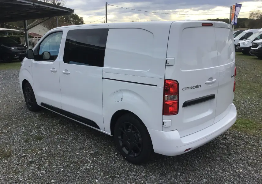 Vue 3/4 arrière côté gauche d'un Citroën Jumpy blanc avec vitres teintées et jantes noires.