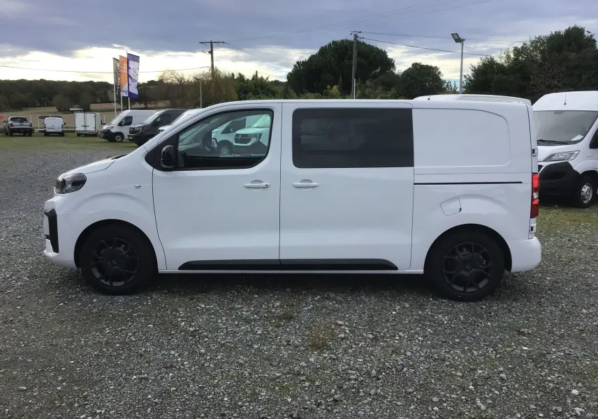 Profil latéral droit d'un Citroën Jumpy blanc avec cabine approfondie et vitres teintées arrière sur parking extérieur.