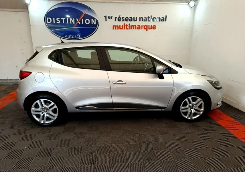 Profil latéral droit d'une Renault Clio Business TCe 90 gris clair, stationnée en intérieur avec jantes alliage visibles.