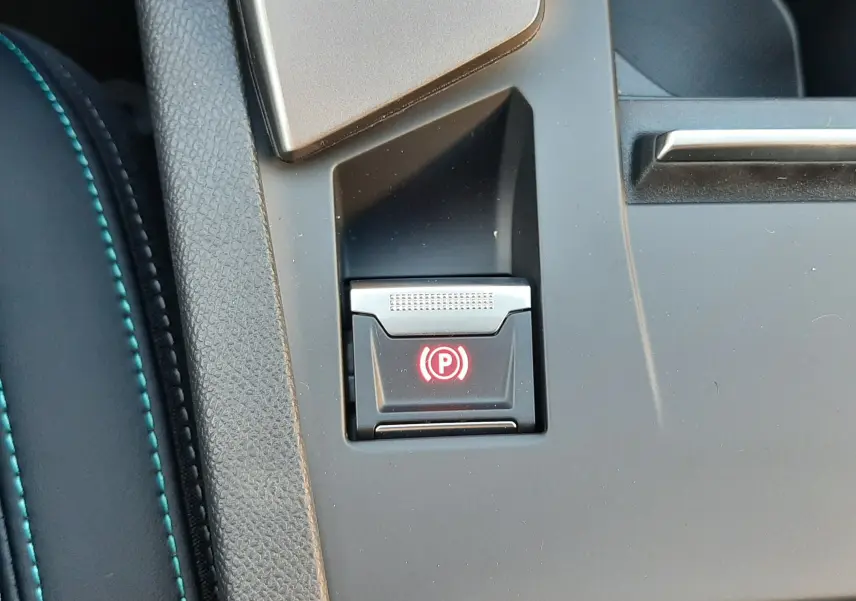 Gros plan sur le bouton de frein à main électronique rouge dans la console centrale noire du Peugeot 308 Bleu Obsession.