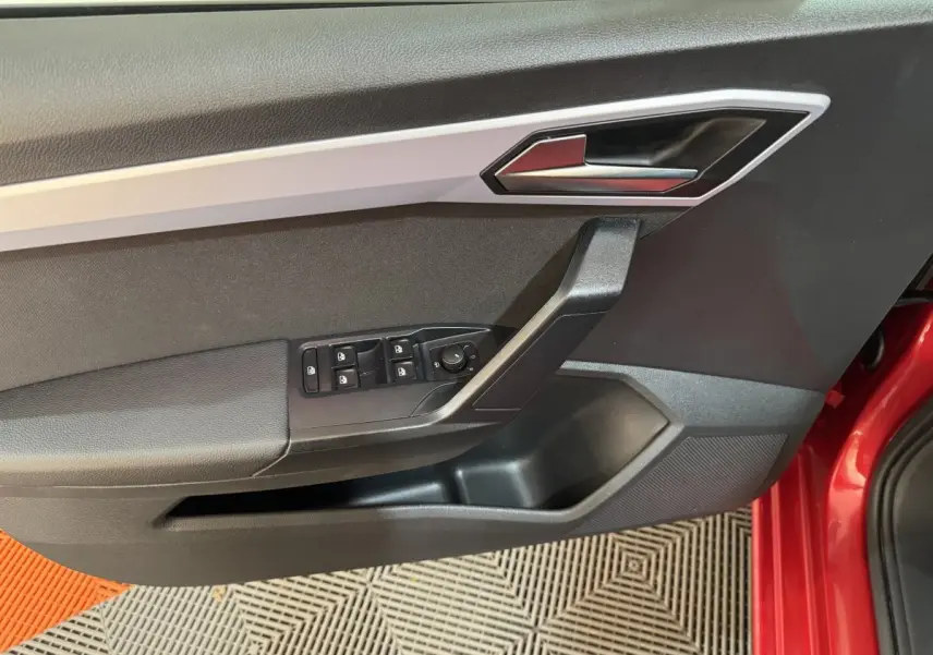 Gros plan sur la porte avant gauche intérieure noire avec commandes électriques sur SEAT Ibiza rouge 2024.