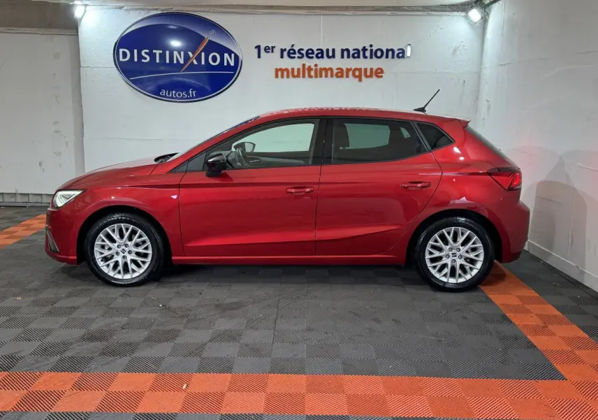 Profil droit d'une SEAT Ibiza 1.0 TSI 110 FR rouge garée en intérieur sur sol à damiers gris et orange.