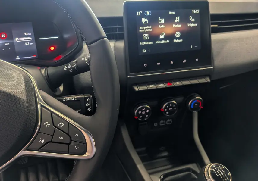 Vue intérieure rapprochée côté conducteur de la Renault Clio V Bleu Iron, avec volant, écran tactile et levier de vitesse manuel visible.