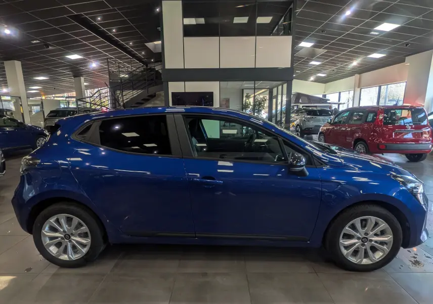 Profil latéral droit de la Renault Clio V bleu Iron 2025 en showroom, avec jantes alliage et vitres teintées.