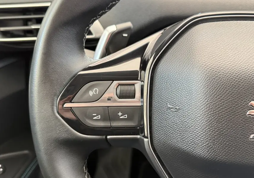 Gros plan sur les commandes gauche du volant cuir noir du Peugeot 3008 gris foncé, avec boutons multifonctions.