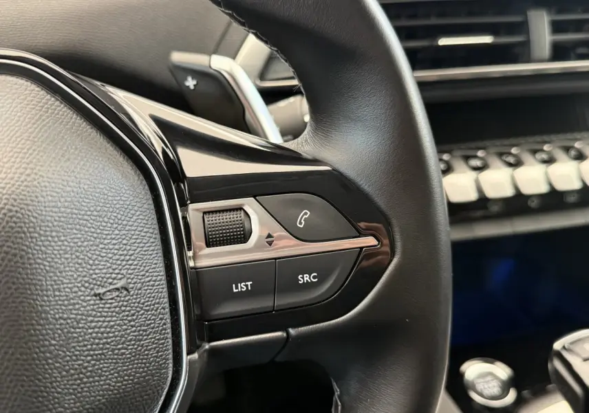 Gros plan sur les commandes gauche du volant cuir noir du Peugeot 3008 2022, avec tableau de bord en arrière-plan.