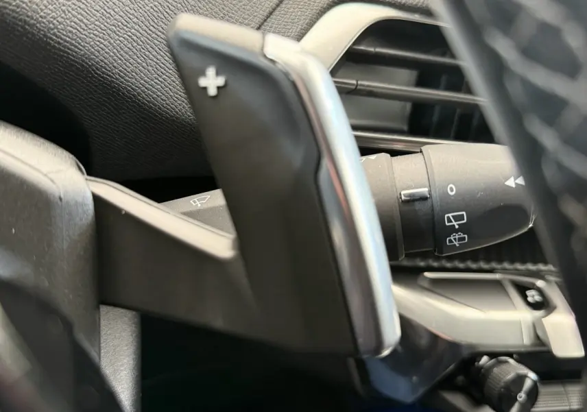 Gros plan sur la palette de changement de vitesse + côté gauche du volant du Peugeot 3008 gris foncé, intérieur moderne.