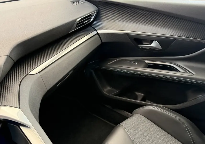Vue intérieure côté passager du Peugeot 3008 gris foncé, mettant en valeur la planche de bord et la porte avec finitions noires et surpiqûres blanches.