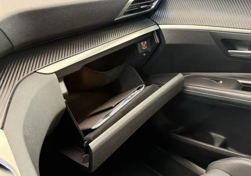 Vue intérieure côté passager du Peugeot 3008 gris foncé 2022 avec boîte à gants ouverte et finition carbone.