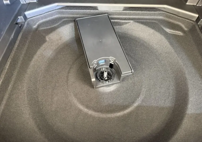 Vue rapprochée de la zone de rangement sous le coffre du Peugeot 3008 gris foncé, montrant un espace vide et un support central.
