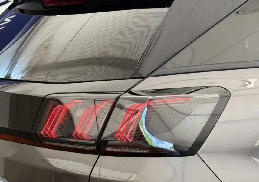 Gros plan sur le feu arrière droit rouge et noir du Peugeot 3008 gris foncé, avec reflet du toit en toile.