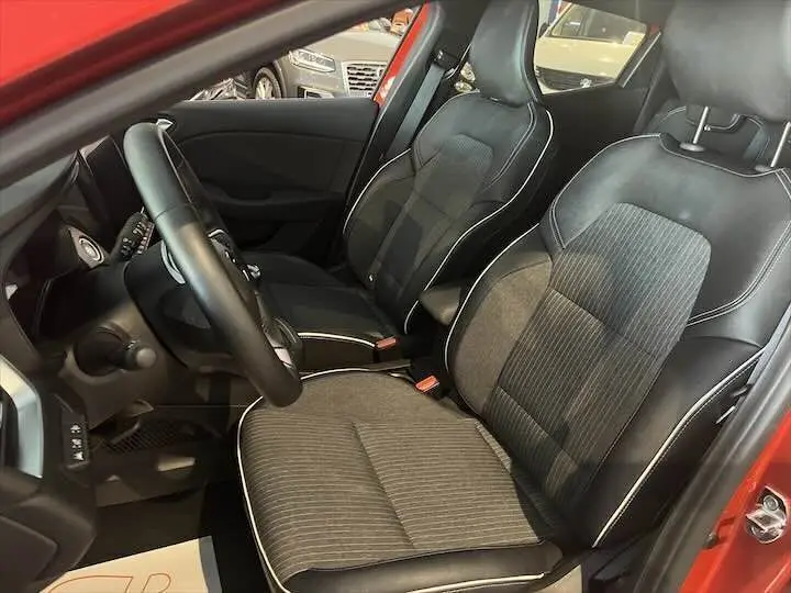 Vue intérieure côté conducteur de la Renault Clio V rouge flamme, sièges mixtes cuir et tissu noir avec surpiqûres blanches.