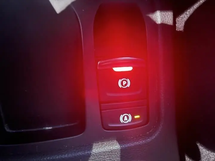 Gros plan sur les commandes électroniques du frein à main et du système start-stop d'une Renault Clio V rouge flamme.