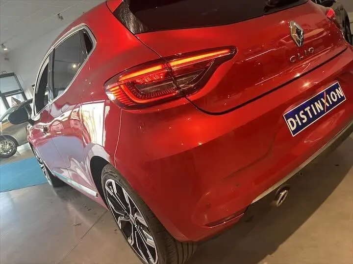 Vue 3/4 arrière droite d'une Renault Clio V rouge flamme métal avec feux LED et jantes alliage noires en showroom.