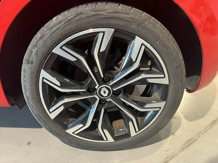 Gros plan sur la jante alliage noire et argentée avec logo Renault, partie avant gauche d'une Clio V rouge flamme.