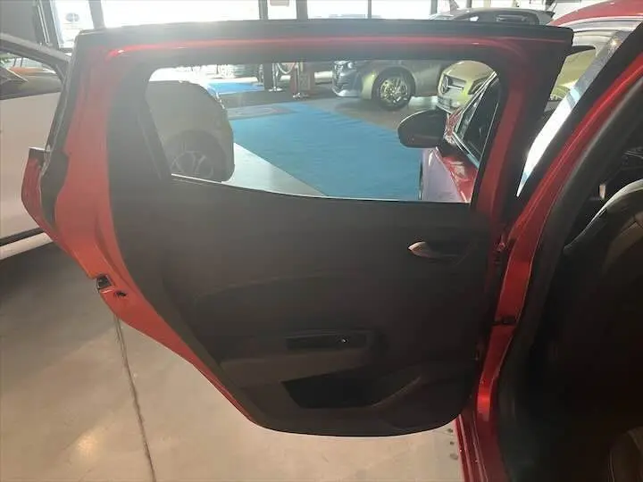 Porte arrière gauche ouverte d'une Renault Clio V rouge flamme métal, montrant l'intérieur sombre et la poignée de porte.