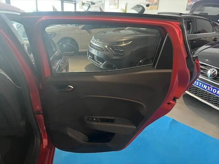 Vue intérieure sur la porte arrière gauche ouverte d'une Renault Clio V rouge flamme métal dans un showroom.