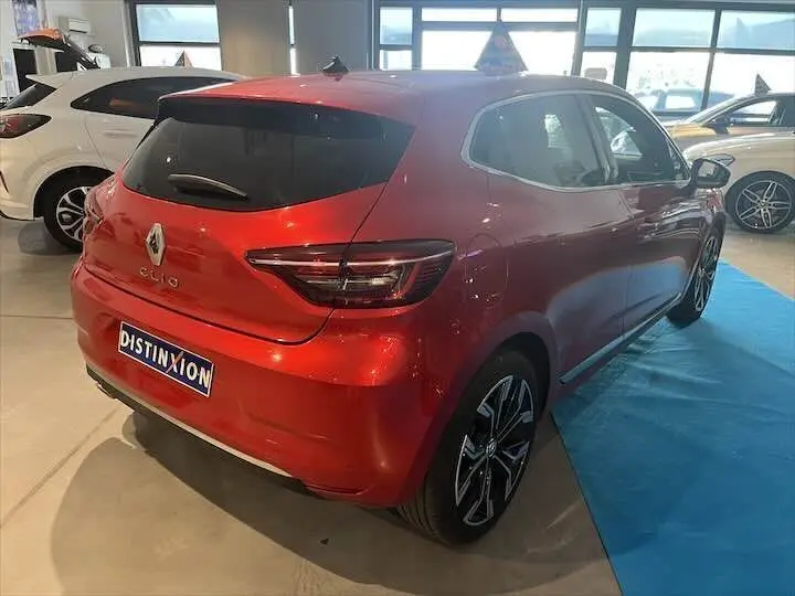 Vue 3/4 arrière droite d'une Renault Clio V rouge flamme métal en showroom avec jantes alliage noires.