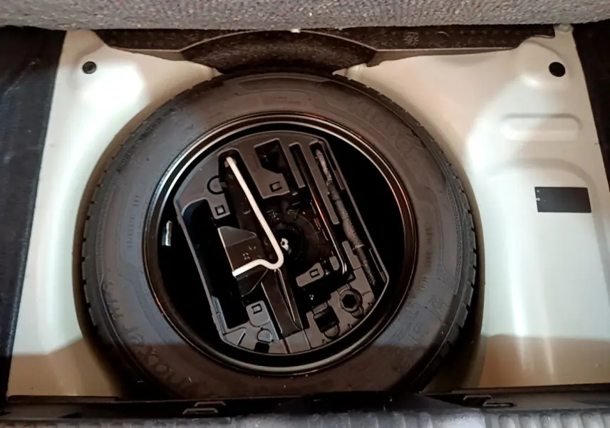 Gros plan sur la roue de secours en jante acier noire dans le coffre blanc d'une Citroën C3 blanche 2019.