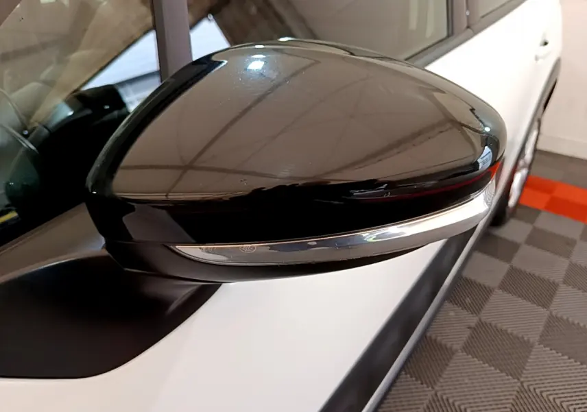 Rétroviseur noir brillant côté gauche d'une Citroën C3 blanche, vue rapprochée sur l'extérieur avant.
