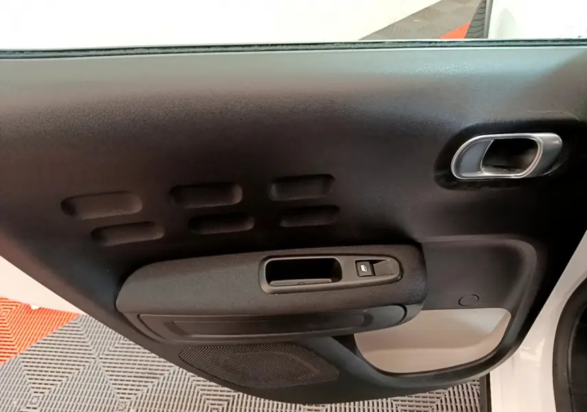 Intérieur côté gauche de la porte avant d'une Citroën C3 blanche, avec poignée noire et bouton de verrouillage.