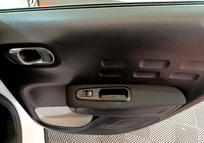 Intérieur côté gauche de la porte avant blanche d'une Citroën C3 2019 avec poignée et commande de vitre noire.