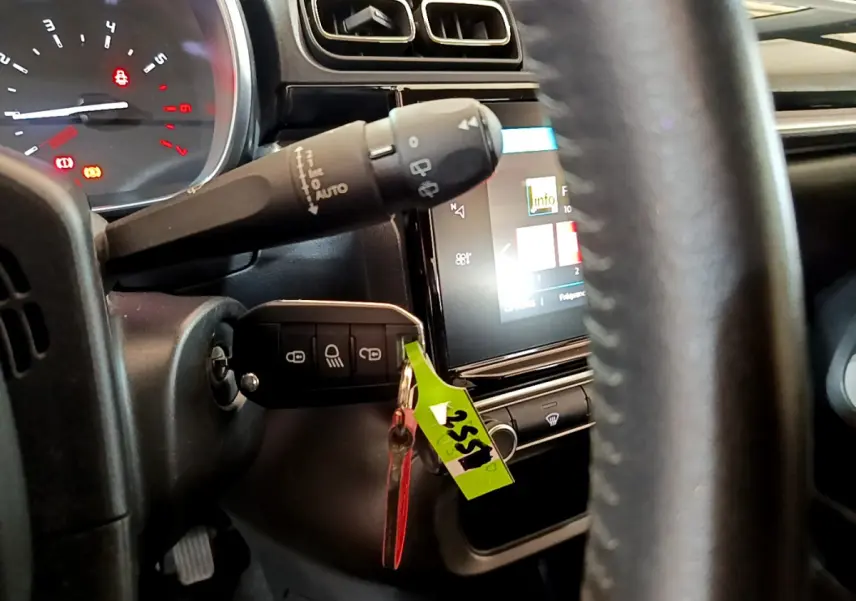 Vue rapprochée du tableau de bord et volant cuir noir de la Citroën C3 blanche avec clé insérée et écran tactile allumé.