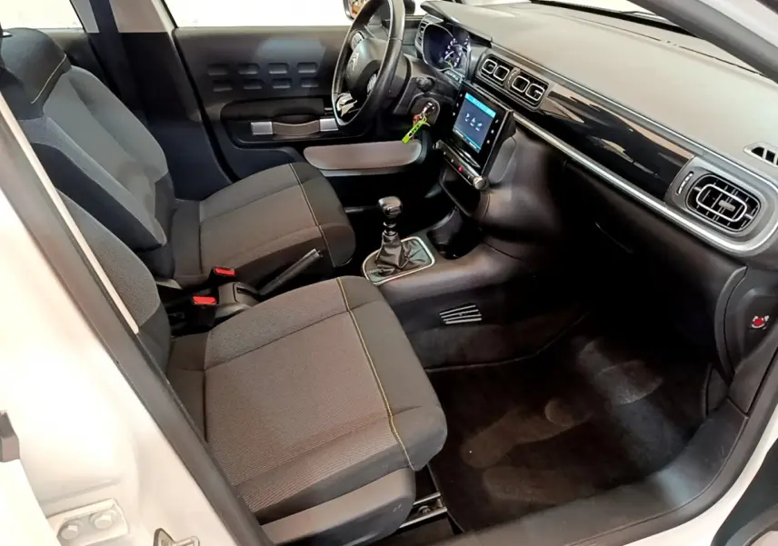 Intérieur avant droit de la Citroën C3 blanche 2019, sièges noirs, tableau de bord avec écran tactile et volant cuir.