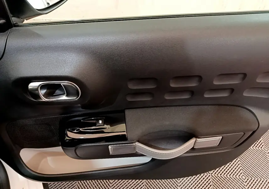 Gros plan sur la porte côté conducteur noire avec poignée argentée et commandes électriques d'une Citroën C3 blanche.