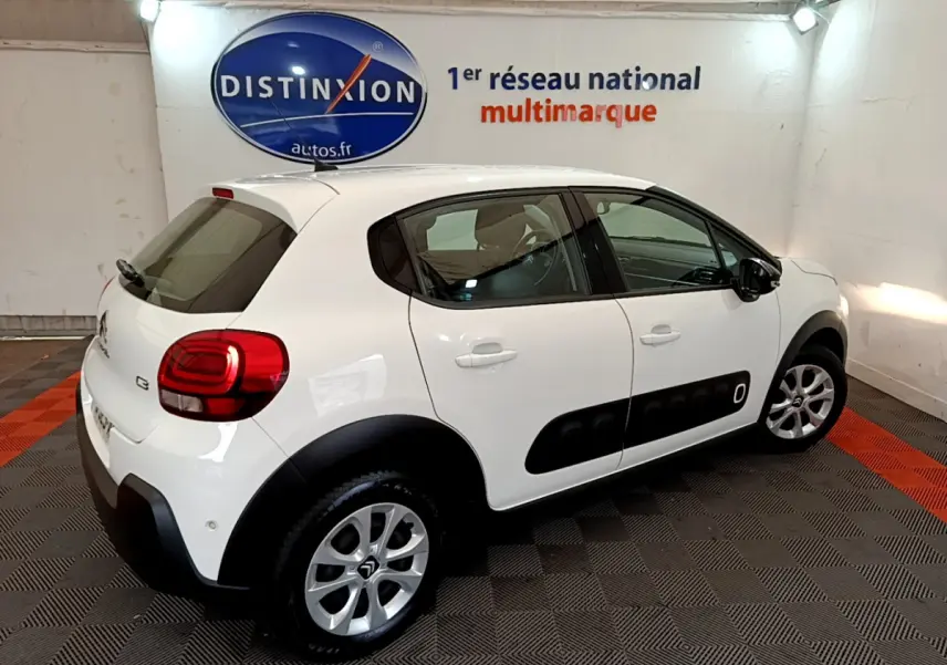 Vue 3/4 arrière droite d'une Citroën C3 blanche avec protections noires latérales et jantes argentées dans un garage.