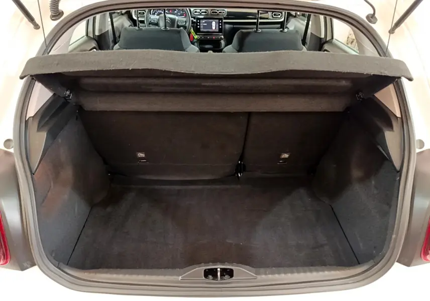 Coffre ouvert de la Citroën C3 blanche vue de l'arrière, avec intérieur noir et tableau de bord visible à travers le pare-brise.