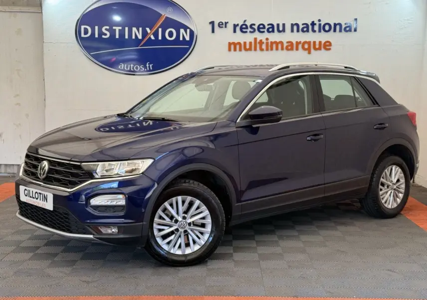 Volkswagen T-Roc bleu en 3/4 avant droit, avec jantes alliage et barres de toit noires visibles.