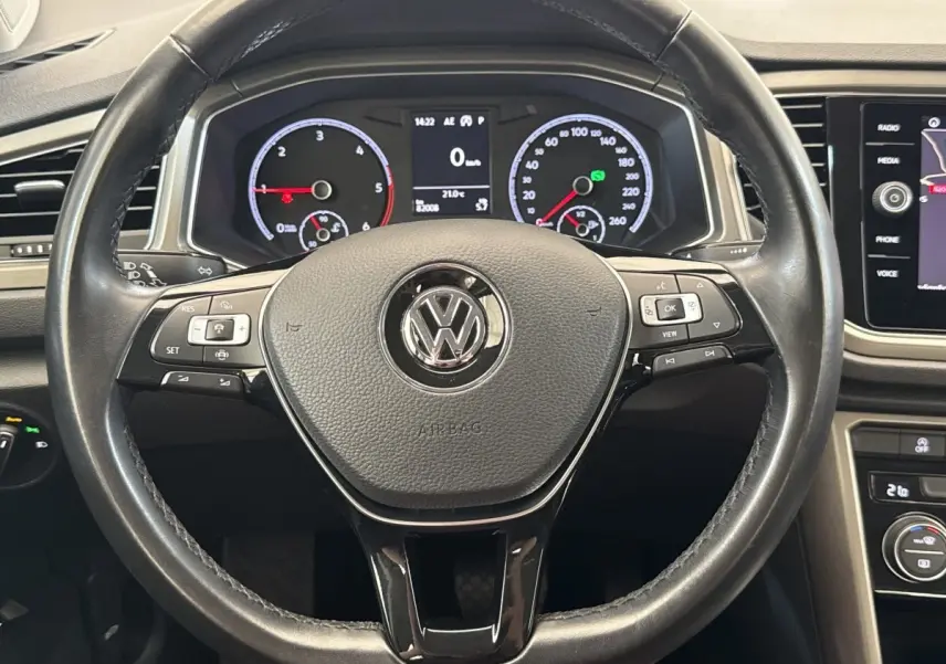 Vue rapprochée du volant cuir noir du Volkswagen T-Roc 2.0 TDI 150, avec tableau de bord numérique et commandes intégrées.