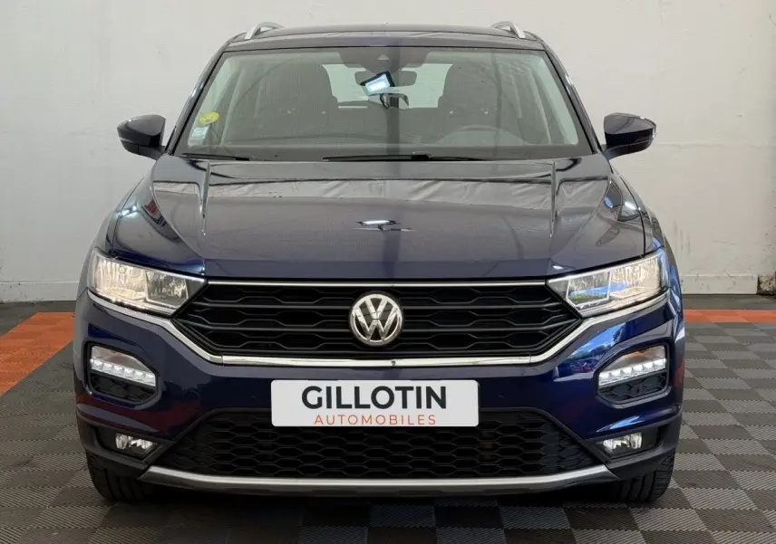Vue avant d'un Volkswagen T-Roc bleu 2020 avec calandre noire et feux LED allumés sur fond intérieur neutre.