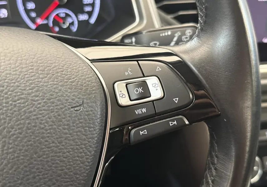 Gros plan sur les commandes multifonctions noires et argent du volant cuir du Volkswagen T-Roc 2.0 TDI bleu, tableau de bord en arrière-plan.
