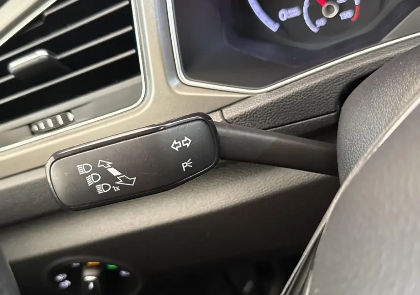 Gros plan sur la commande de clignotants et feux à gauche du volant dans l’habitacle du Volkswagen T-Roc bleu.
